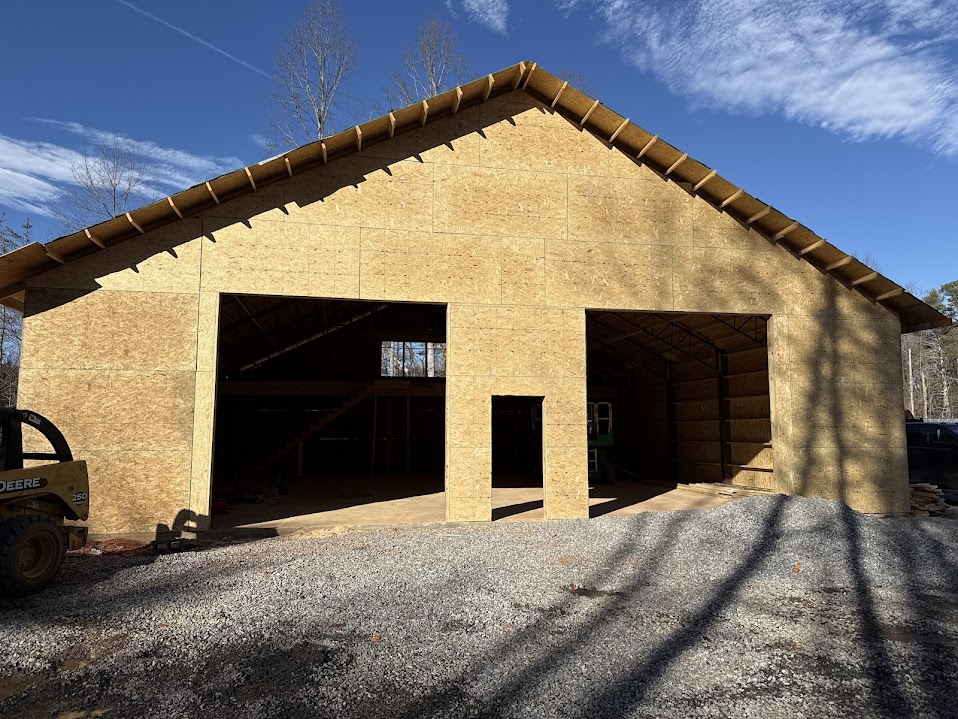 Gabled barn workshop during framing with exposed sheathing and rough openings for two bay doors and a pedestrian door