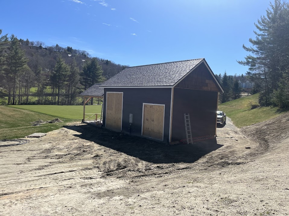 Small gray-sided shed with a shingle roof and covered entry on a graded site