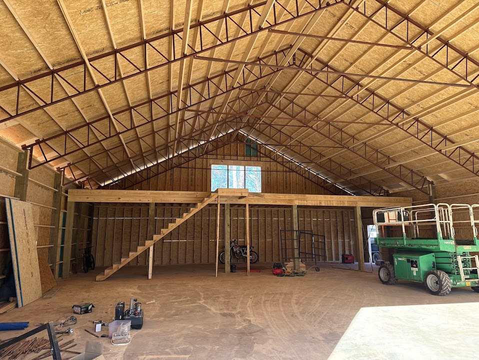 Barn interior with exposed trusses, OSB sheathing, and a loft stair under construction