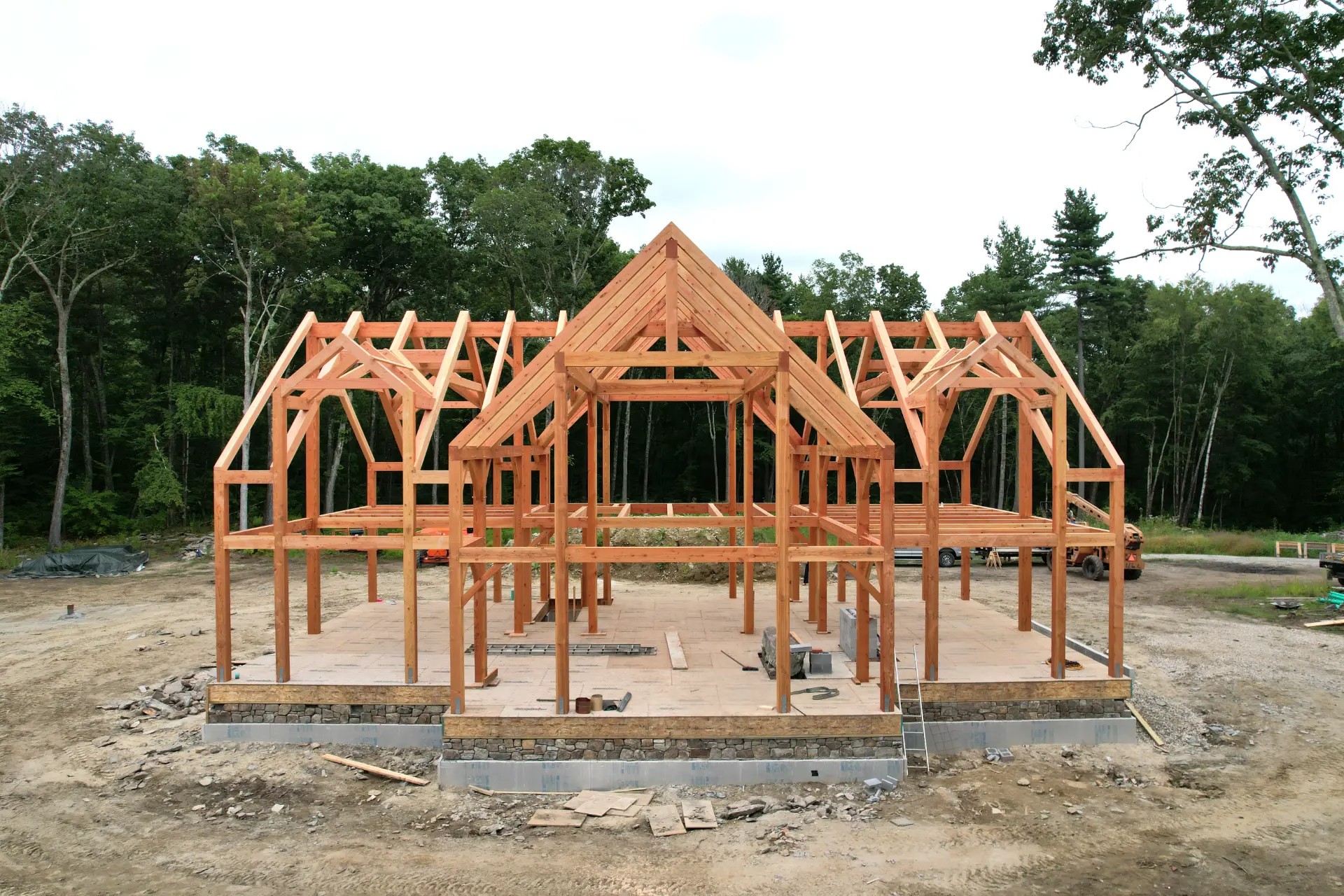 Heavy timber frame with mortise-and-tenon joinery and knee braces rising over a stone foundation