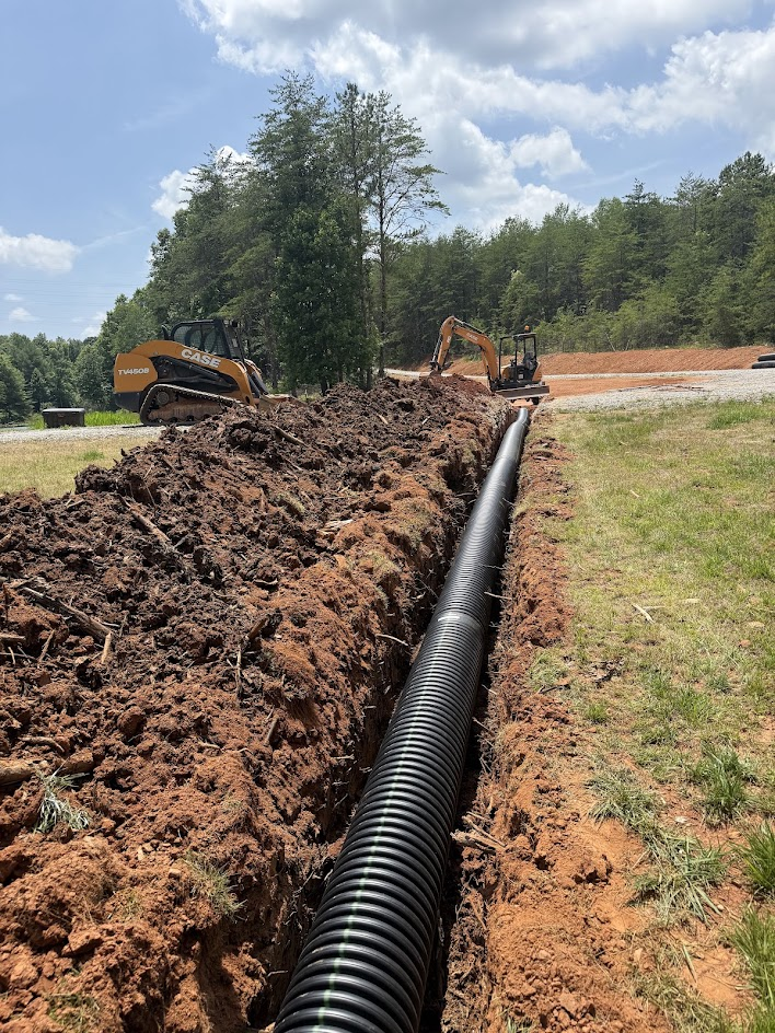 Trench with black corrugated drainage pipe beside a skid steer and mini excavator