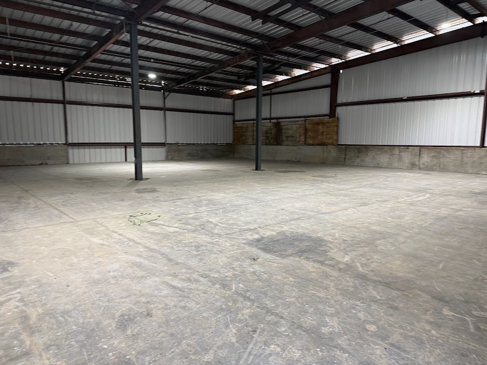Interior of a steel-frame building with a poured concrete slab, white metal wall panels, dark steel columns, and a metal roof deck with skylights