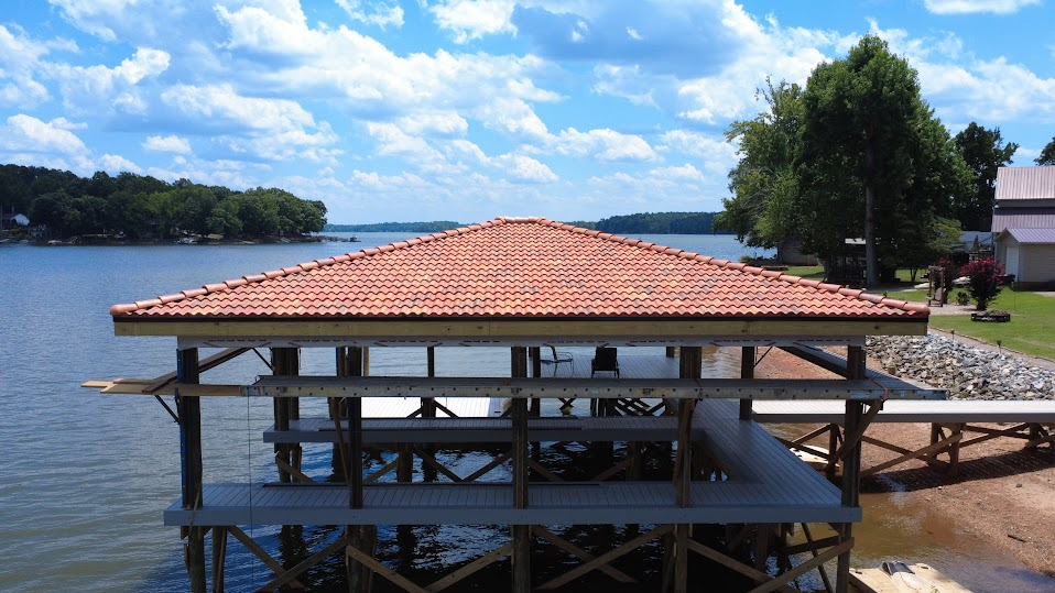 Aerial view of a lake boathouse with a red tile roof and floating docks