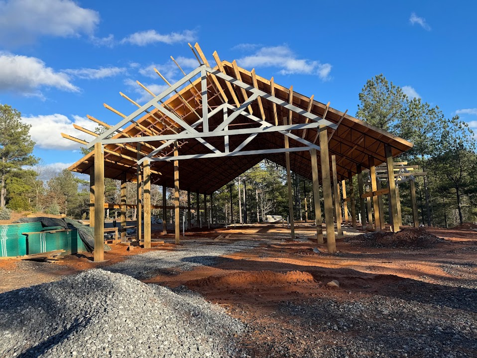 Post-frame pole barn under construction with a painted steel gable truss and wood purlins