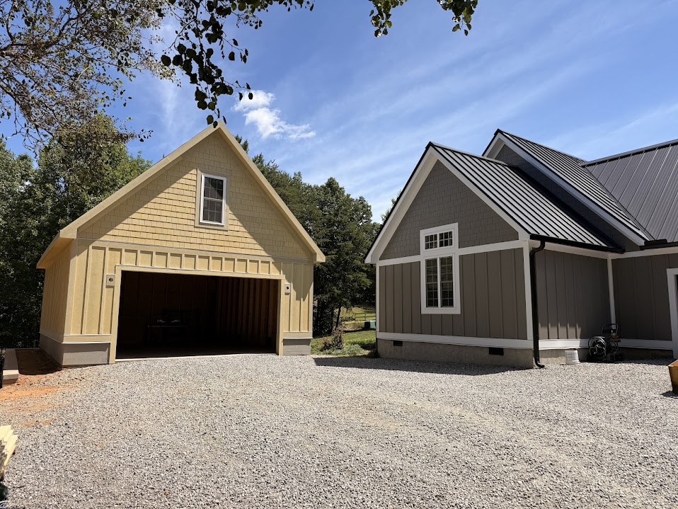 Detached garage nearing completion with pale yellow shingle and board-and-batten siding beside a finished house