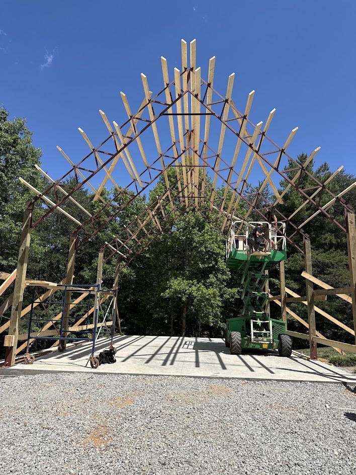 Wood posts supporting steel open-web trusses under a gable roof on a wooded site